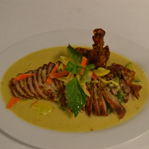 Siri Thai Cuisine's roasted duck in green curry, garnished with basil, carrots, and lime.