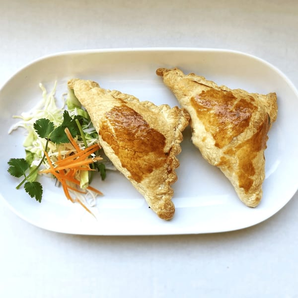 Two golden-brown curry puffs with a side of shredded cabbage, carrots, and cilantro.