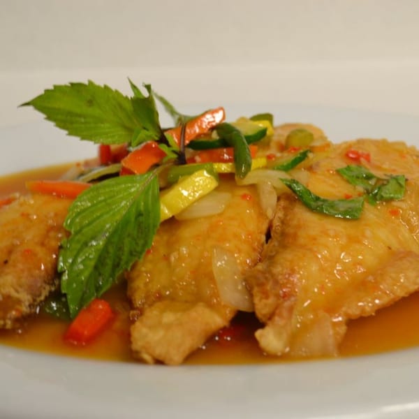 Crispy Thai fish fillets with sweet chili sauce, bell peppers, zucchini, and basil on a white plate.