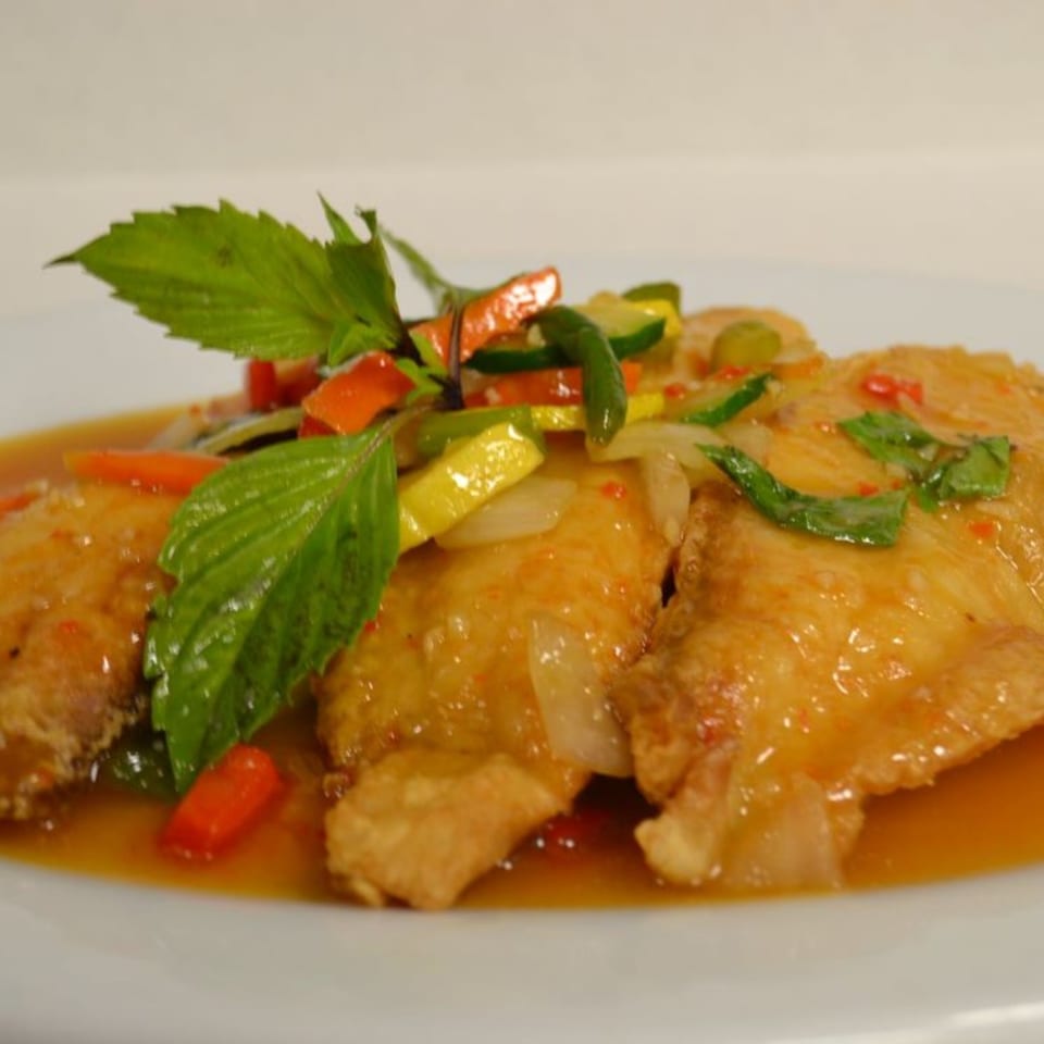 Crispy Thai fish fillets with sweet chili sauce, bell peppers, zucchini, and basil on a white plate.