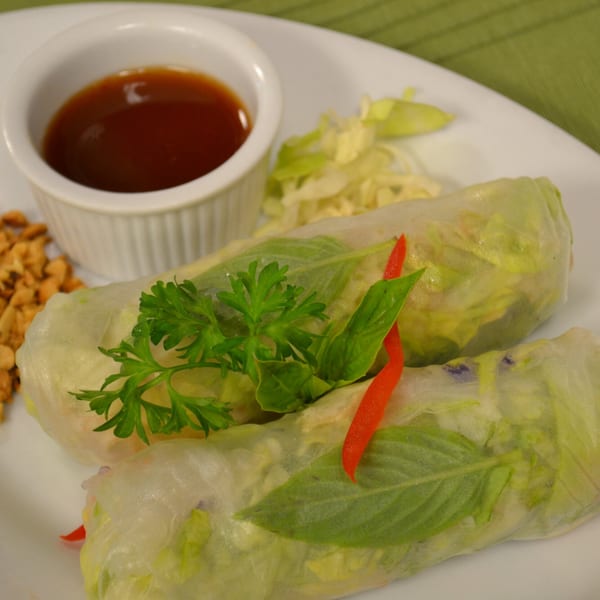 Two fresh spring rolls with herbs, a side of chopped peanuts, and a dipping sauce.