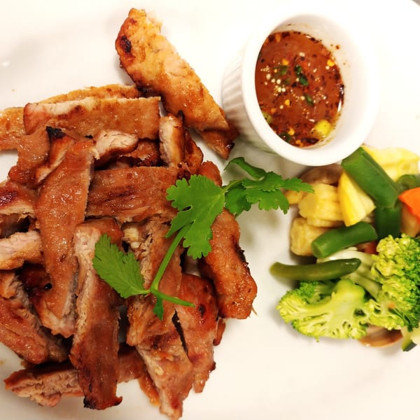 Grilled pork slices with cilantro, a side of mixed vegetables, and a dipping sauce.