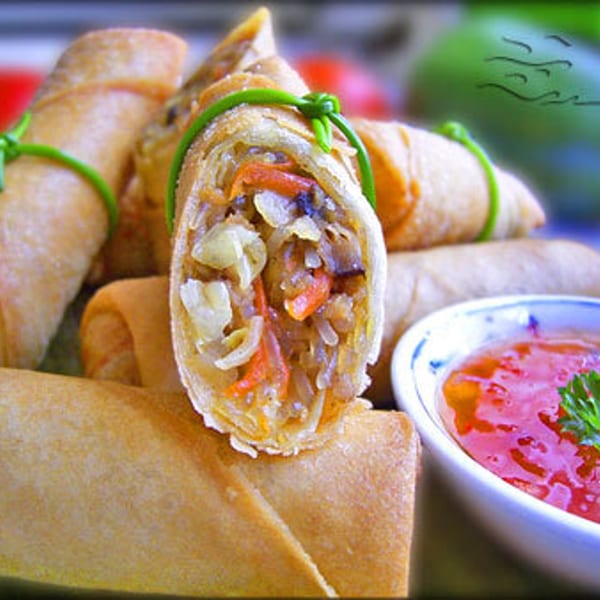 Crispy Thai spring rolls, one cut open to show vegetable filling, with sweet chili dipping sauce.